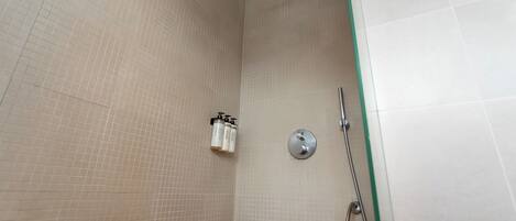 Un espace douche avec des murs carrelés, une douchette à main et un robinet fixé au mur.