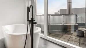 Une salle de bain moderne avec une baignoire blanche, un robinet noir et une grande fenêtre donnant sur le toit.