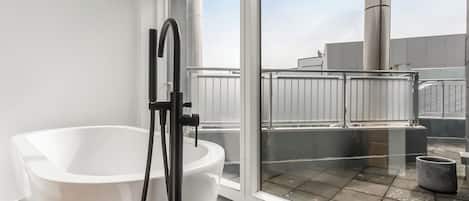 Ein modernes Badezimmer mit einer weißen Badewanne, einem schwarzen Wasserhahn und einem großen Fenster mit Blick auf das Dach.