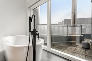 Een moderne badkamer met een witte badkuip, een zwarte kraan en een groot raam met uitzicht op het dak.