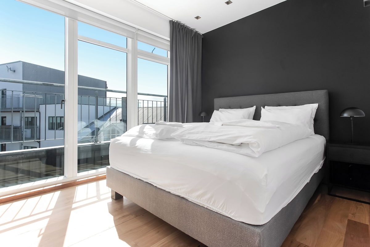 Un dormitorio moderno con una cama grande, vistas a un balcón y una pared oscura.