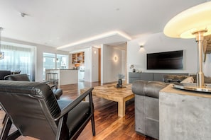 A modern living room with a leather sofa, a wooden coffee table, and a TV mounted on the wall.