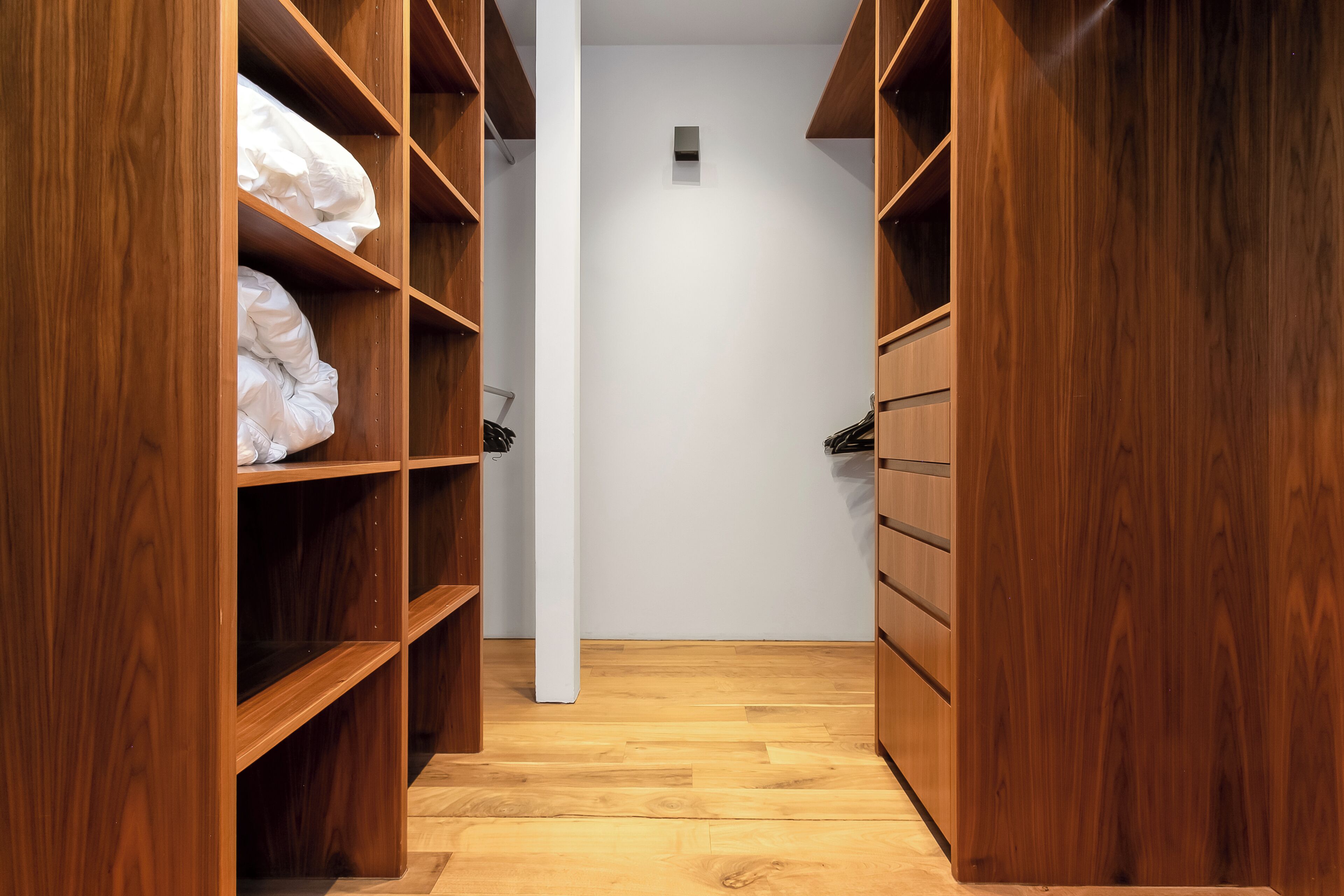A wooden closet with shelves and drawers, a white wall, and a wooden floor.