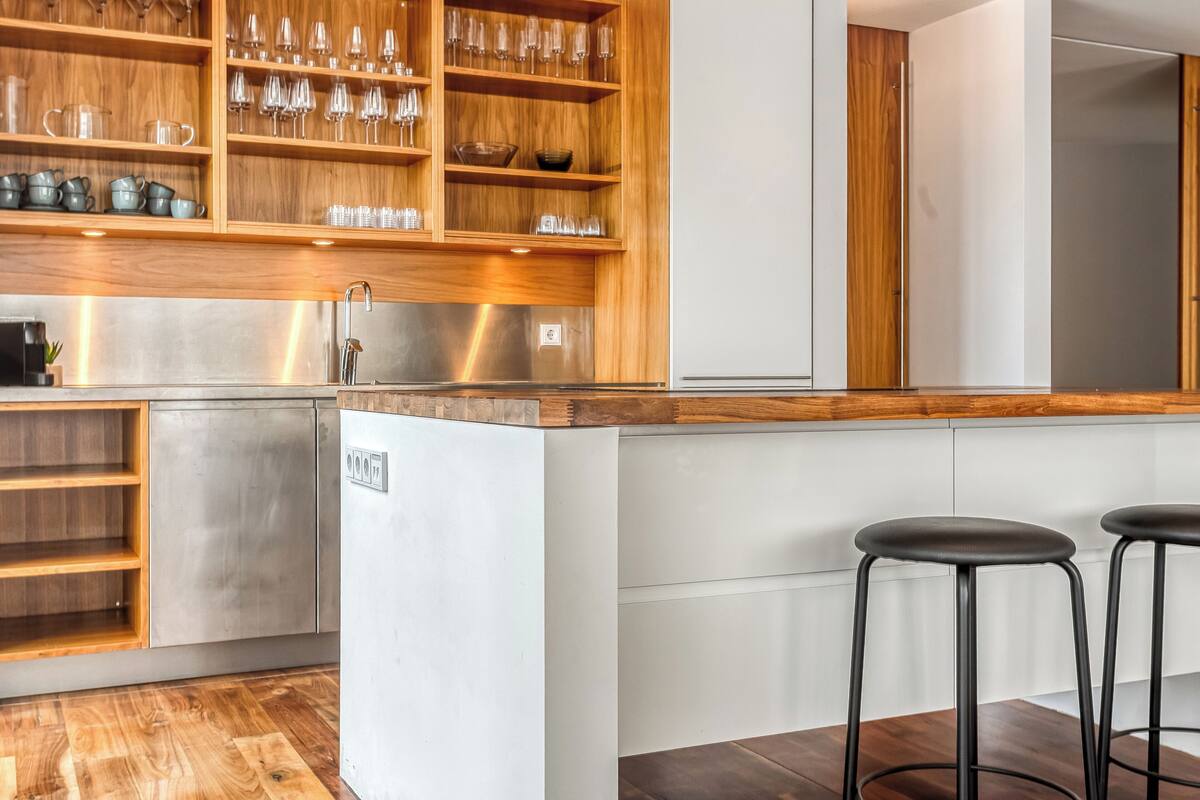 Una cocina moderna con estantes de madera, electrodomésticos de acero inoxidable y dos taburetes negros.