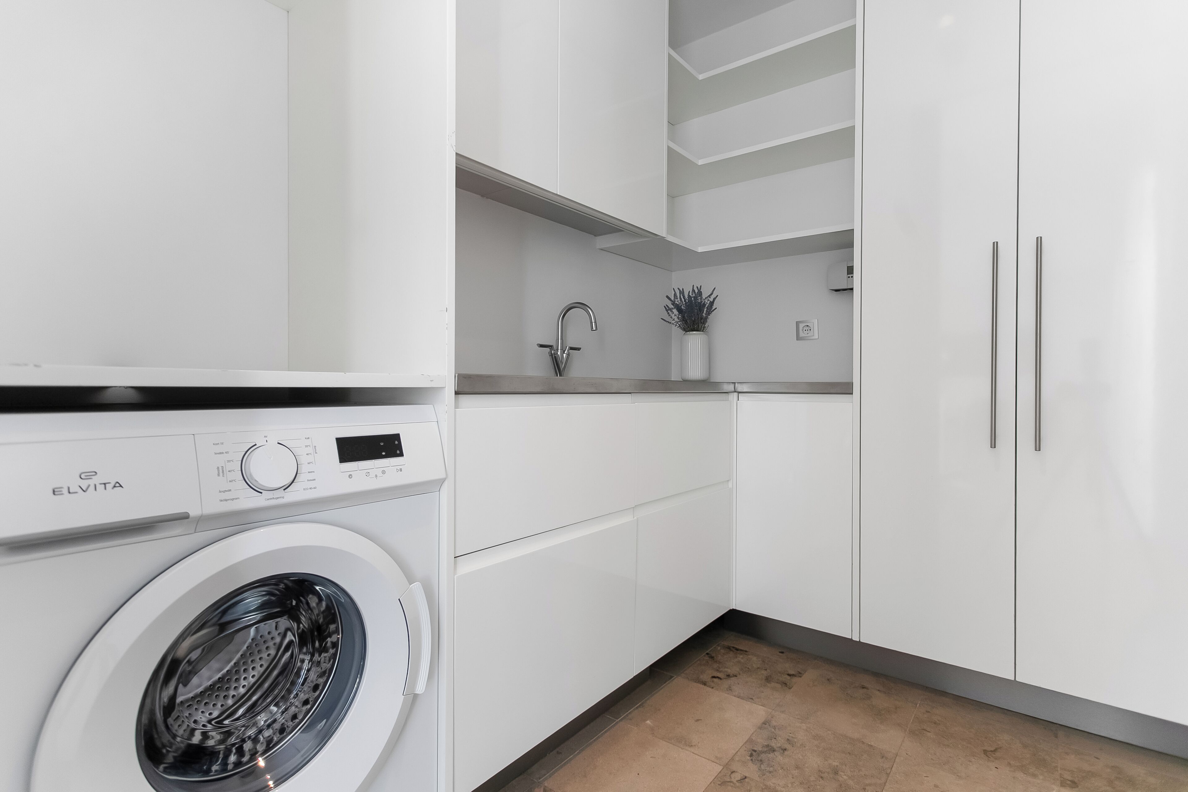 A modern kitchen with a built-in washer, white cabinets, and a small countertop with a sink and plant.