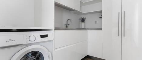 A modern kitchen with a built-in washer, white cabinets, and a small countertop with a sink and plant.