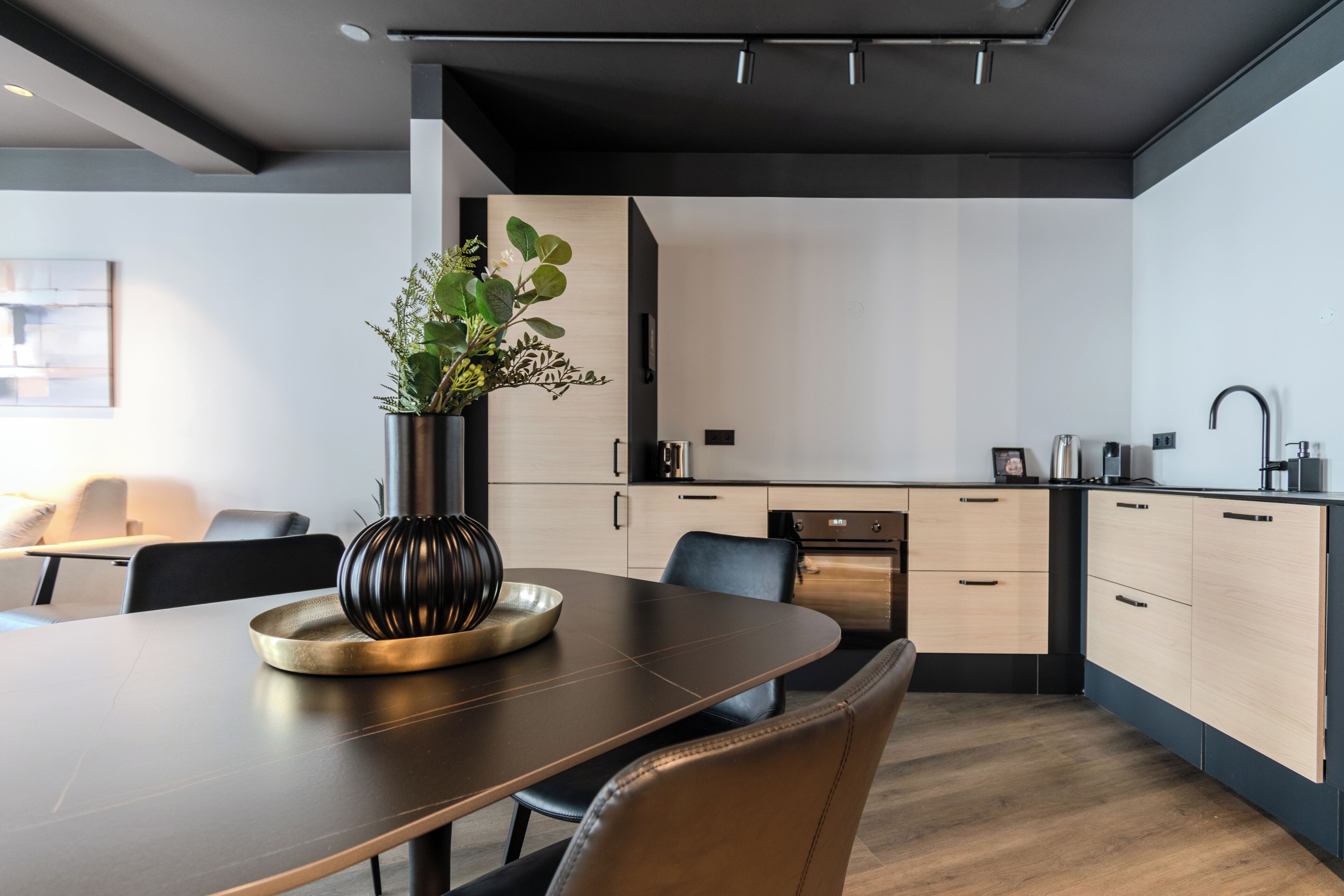 Una cocina moderna con armarios oscuros, un horno de acero inoxidable y un comedor con una mesa y sillas oscuras.