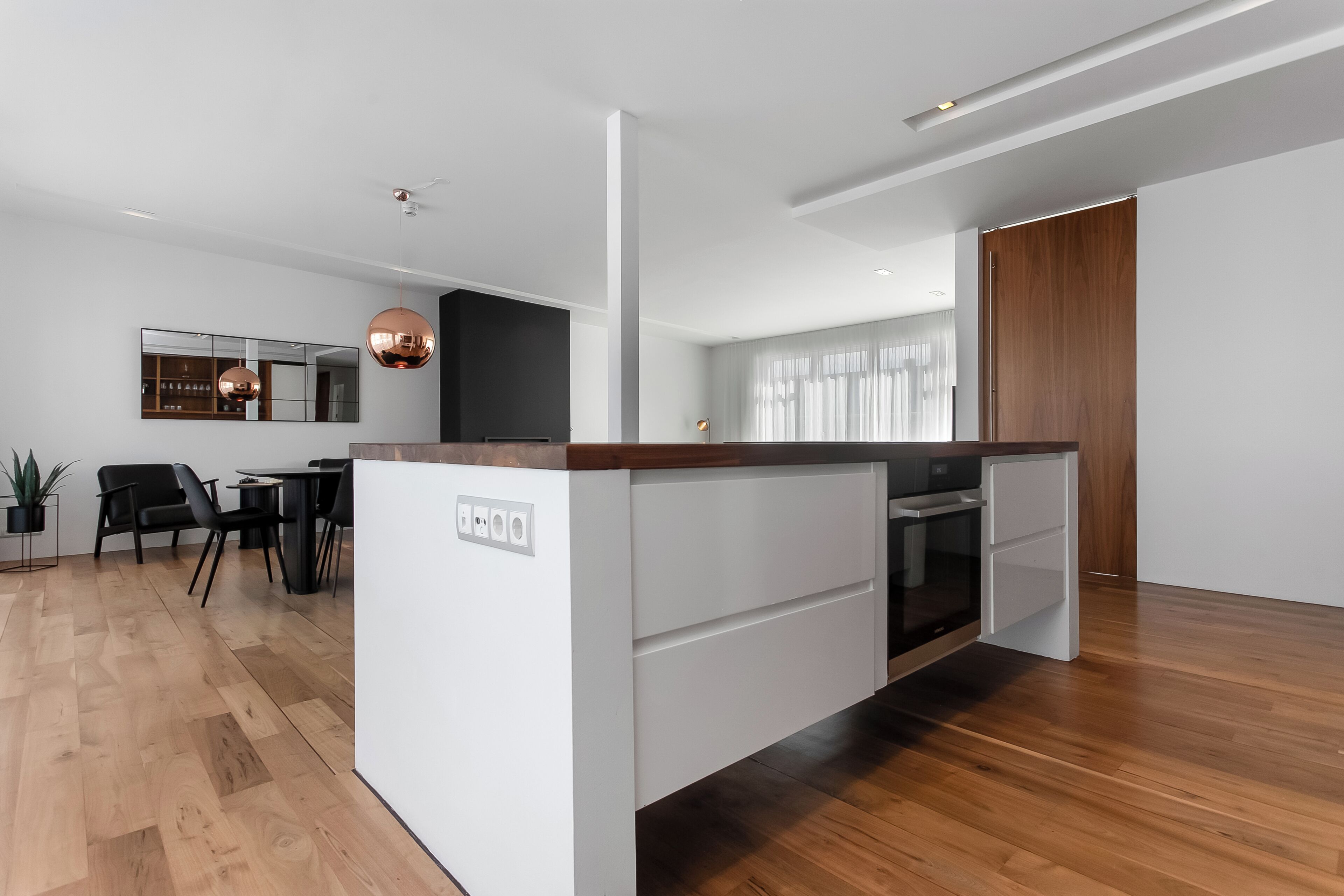 A modern kitchen with a central island, wooden flooring, and a dining area with chairs.