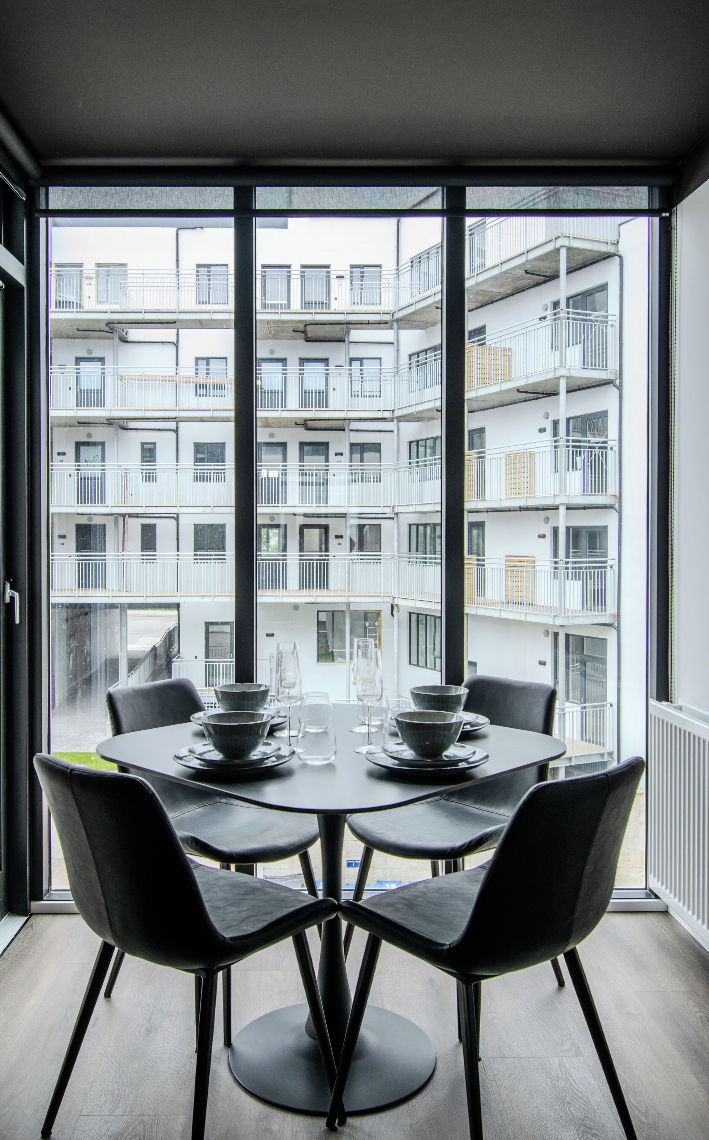A dining area with a table and chairs, large windows with a view of a multi-story building.