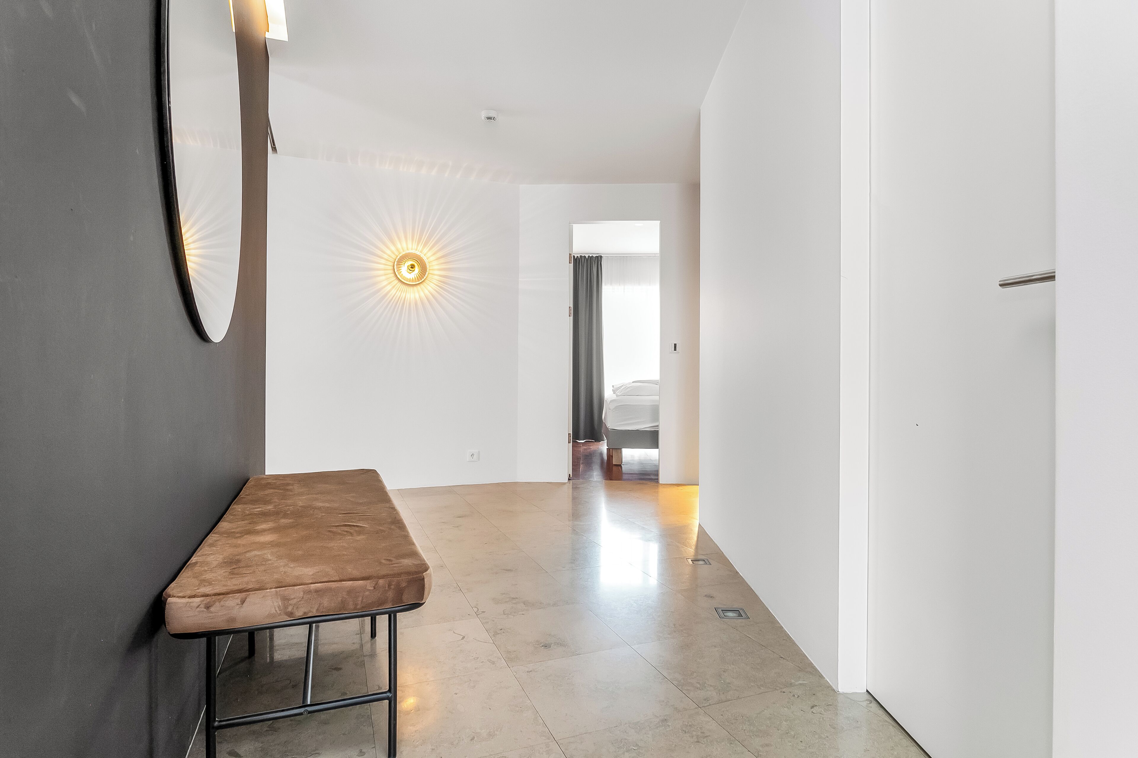 Un pasillo con un banco, una lámpara en la pared y una puerta que da a otra habitación.