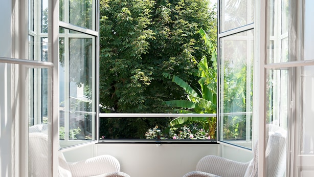A room with a large window overlooking a lush garden. There are two wicker chairs in the room. - Chambres d'Hôtes Eden Ouest (La Rochelle)