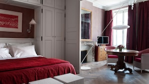 A hotel room with a large bed, a round table with a vase of flowers, a chair, and a dresser. - Chambres d'Hôtes Eden Ouest (La Rochelle)