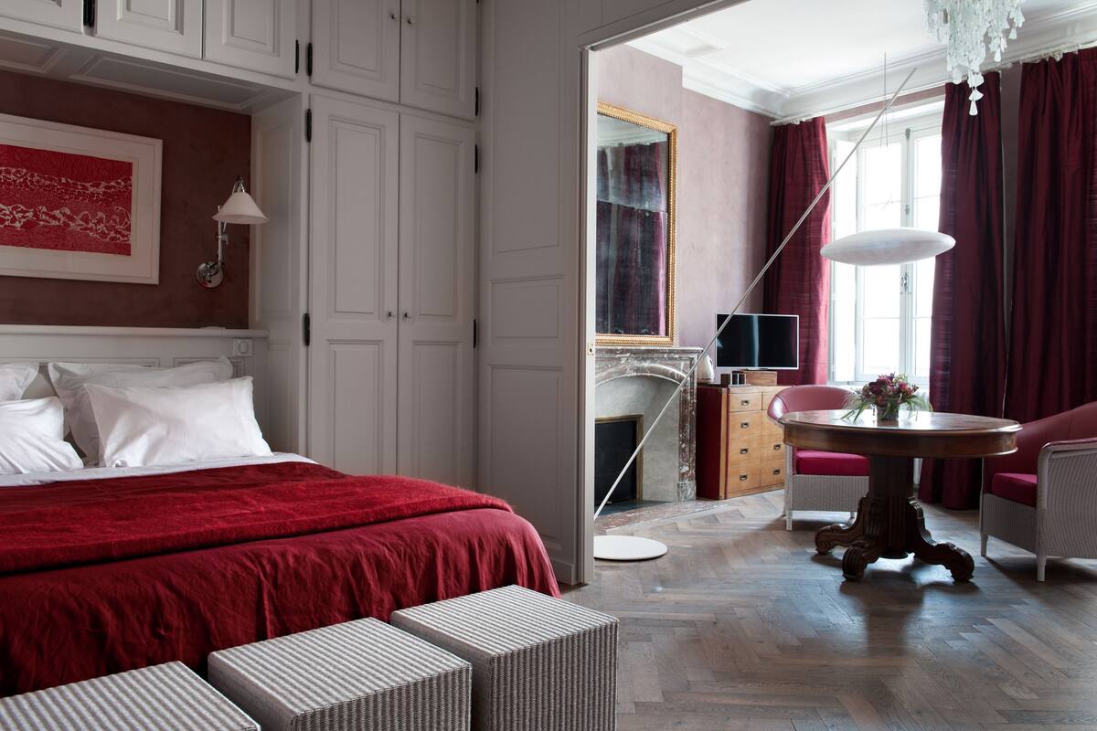 A hotel room with a large bed, a round table with a vase of flowers, a chair, and a dresser.