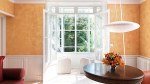 A room with a large open window, a round table with a vase of flowers, and two white chairs. - Chambres d'Hôtes Eden Ouest (La Rochelle)