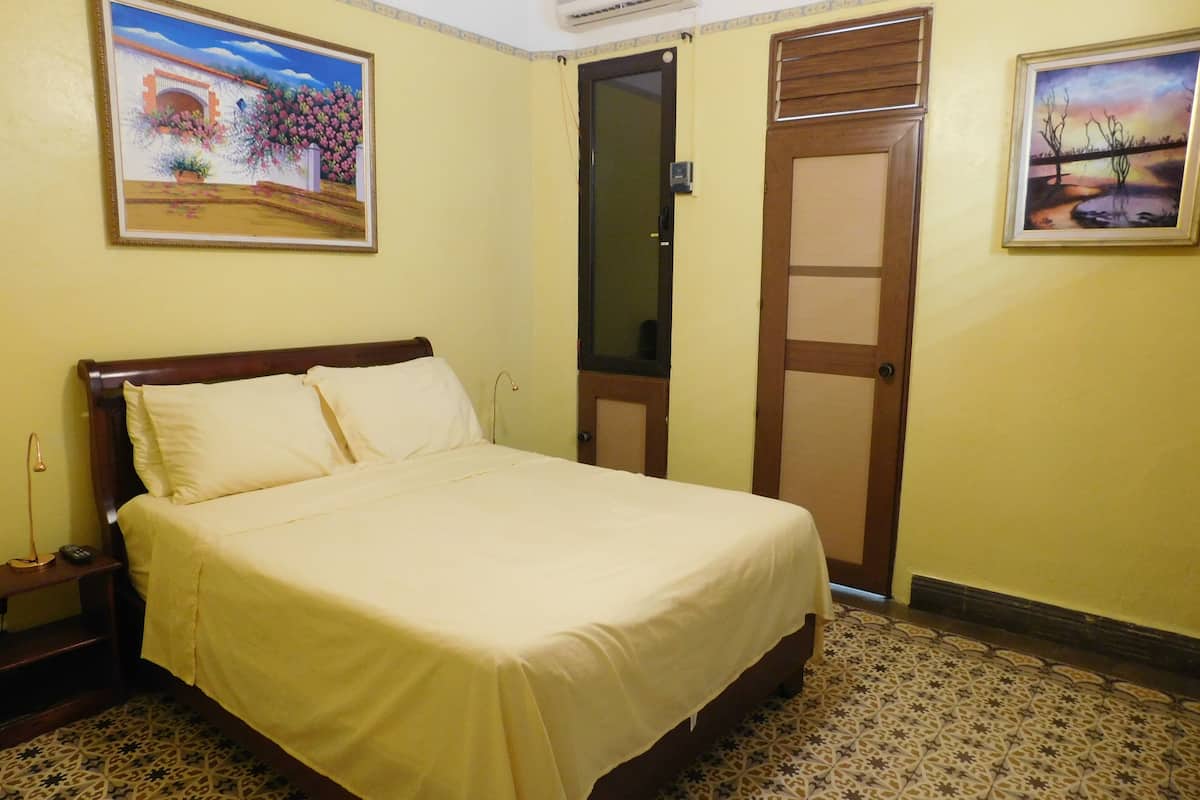 A hotel room with a bed, a nightstand, a wall-mounted air conditioner, and two doors.