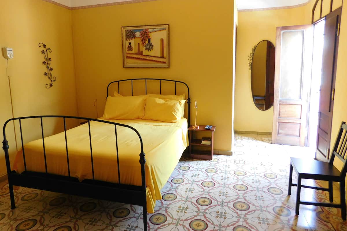 A bedroom with a bed, a nightstand, a chair, a mirror, and a door.