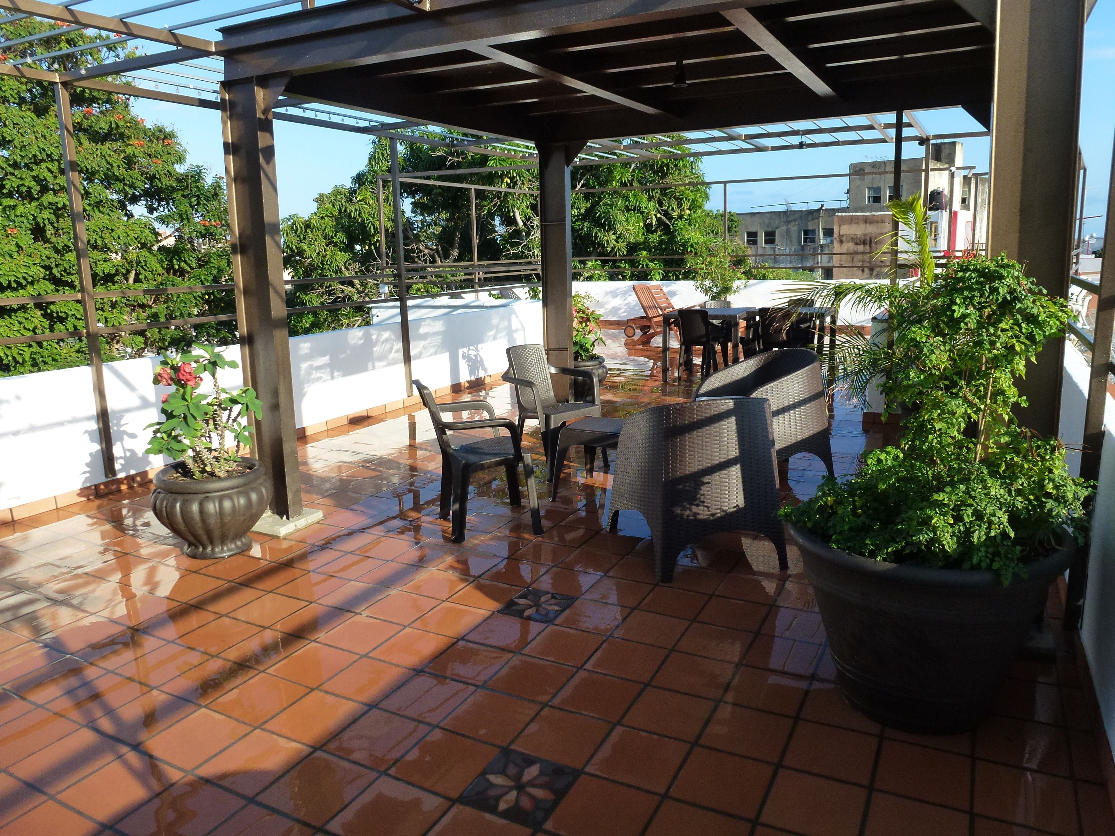 A covered patio area with tiled flooring, outdoor furniture, and potted plants.