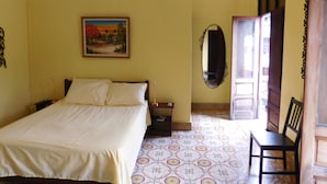 Un dormitorio con cama, mesita de noche, espejo, silla y puerta que da a otra habitación.