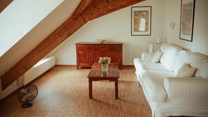 Une chambre à coucher confortable, aménagée en mezzanine, avec un plafond en pente, un canapé blanc, une table en bois ornée d’un vase et un meuble de rangement.