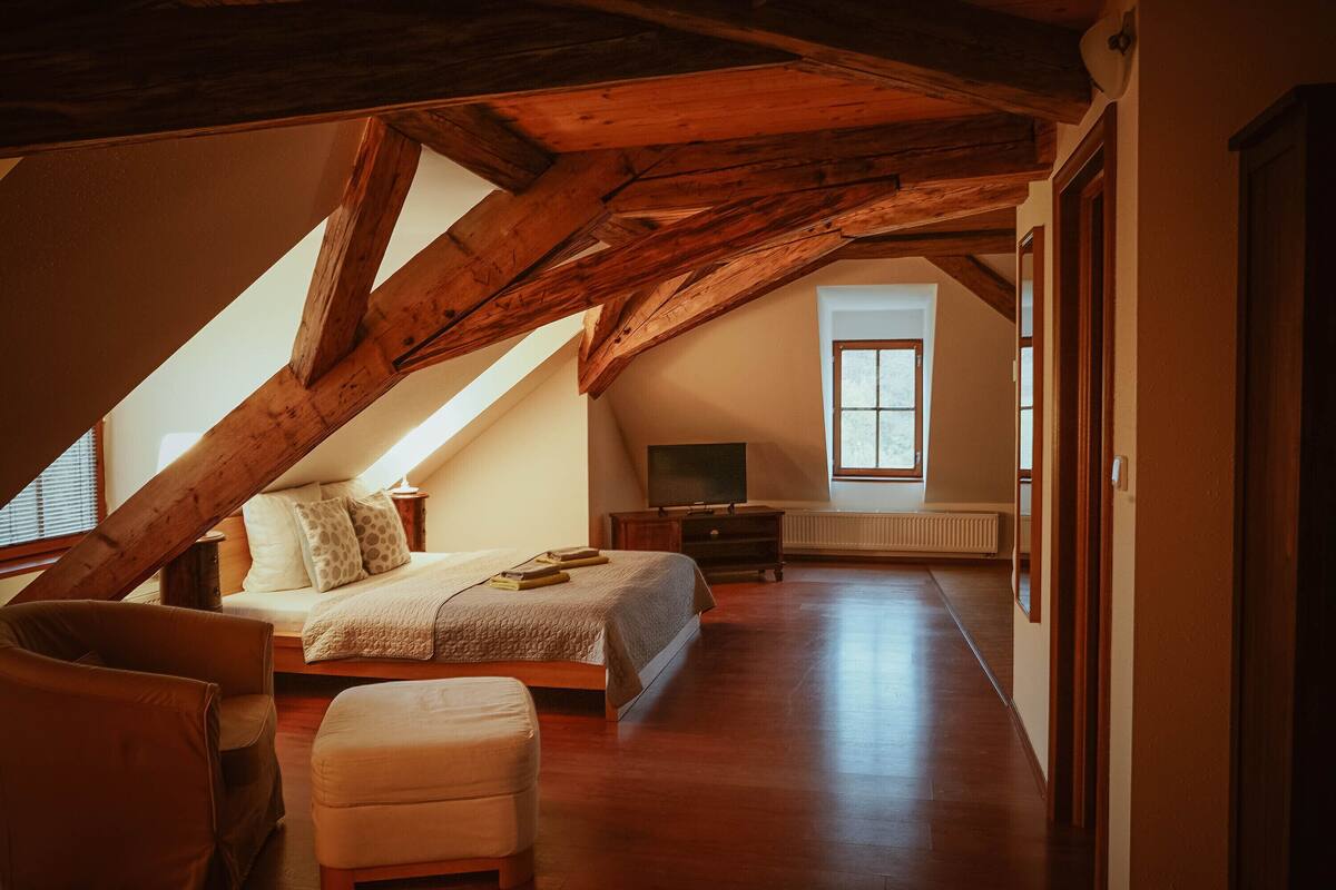 A spacious attic bedroom with a sloped ceiling, a large bed, a TV, and a view of the outdoors.
