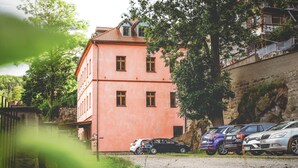 Un bâtiment rose avec de nombreuses fenêtres, des voitures garées et un mur en pierre.