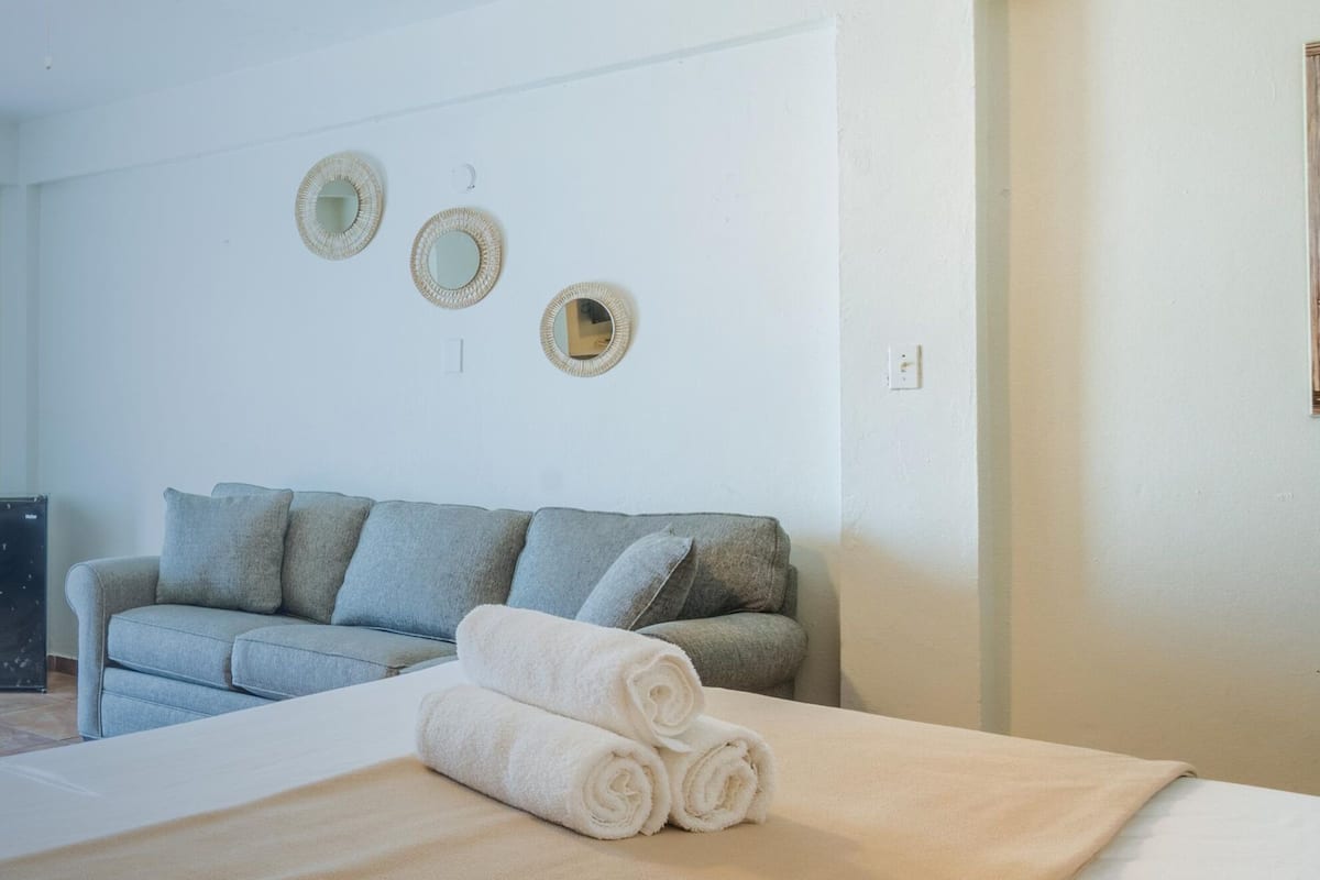 A bedroom with a large bed, a grey sofa, and two wall-mounted mirrors.