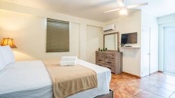 A hotel room with a bed, a dresser, a television, and an air conditioning unit.