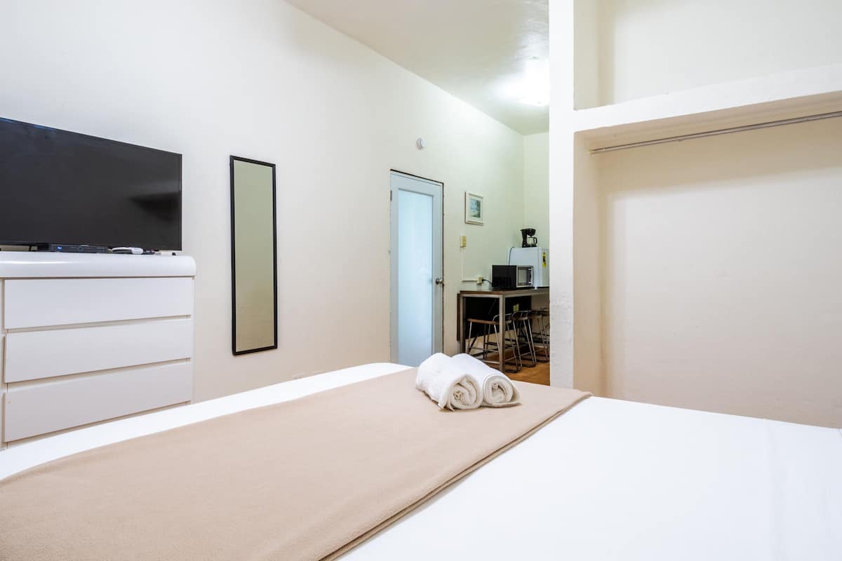 A hotel room with a bed, a TV, a dresser, and a desk with a chair.