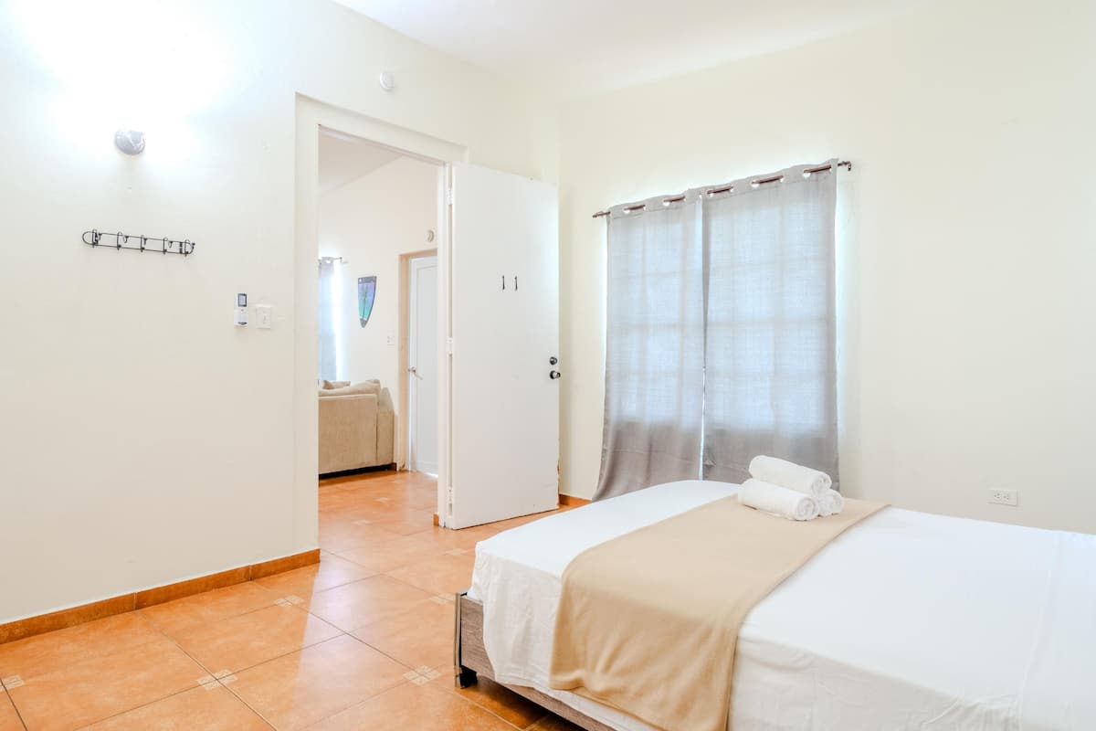 A hotel room with a bed, a bathroom visible through an open door, and a window with curtains.