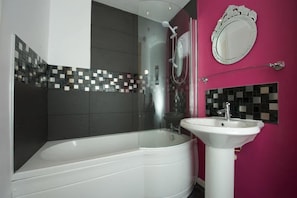 A modern bathroom with a glass-enclosed shower, a white bathtub, and a white sink against a pink wall.