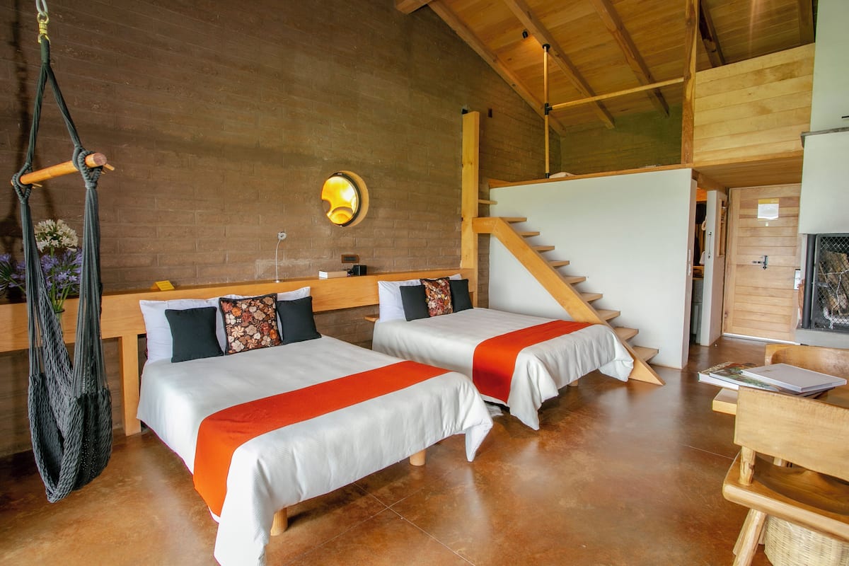 A room with two beds, a hanging chair, a staircase, and a wooden ceiling.