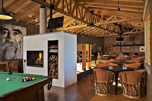 A cozy indoor space with a pool table, a fireplace, and wooden tables and chairs.