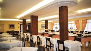 Een eetgedeelte met meerdere tafels en stoelen, grote pilaren en een buffetopstelling.