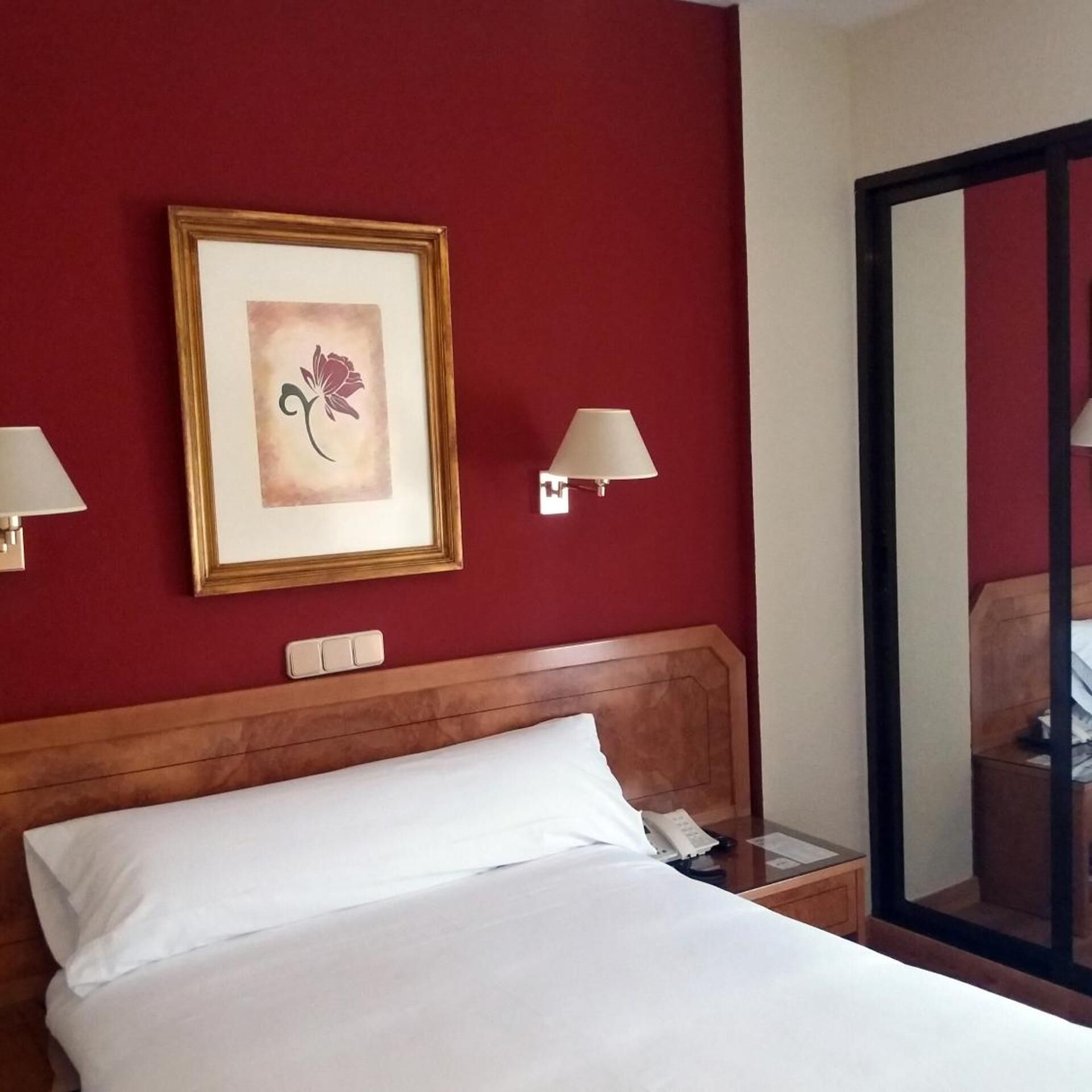 Una habitación de hotel con una cama, una obra de arte enmarcada, lámparas de noche, una mesita de noche y un espejo.