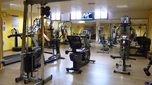 Et fitnessrum med diverse træningsmaskiner, en spejlvæg og et fjernsyn på væggen.