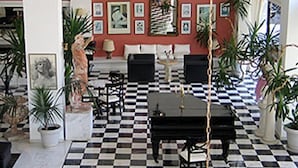 A lobby with a checkered floor, a piano, seating arrangements, and framed artwork on the walls. - Venus Melena (Hersonissos)
