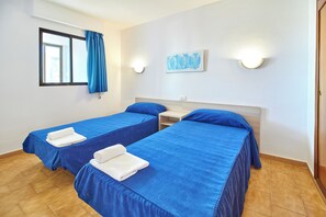 A hotel room with two single beds, a window with blue curtains, a wall-mounted light, and a painting. - Don Gregorio - Fincas Benidorm (Benidorm)