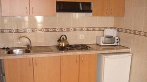 A kitchen with wooden cabinets, a gas stove, a kettle, a toaster, and a white refrigerator.