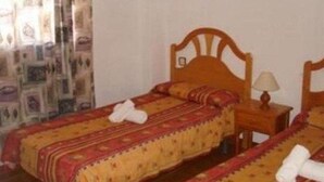 A hotel room with two single beds, each with a wooden headboard, a bedside table with a lamp, and a patterned bedspread.