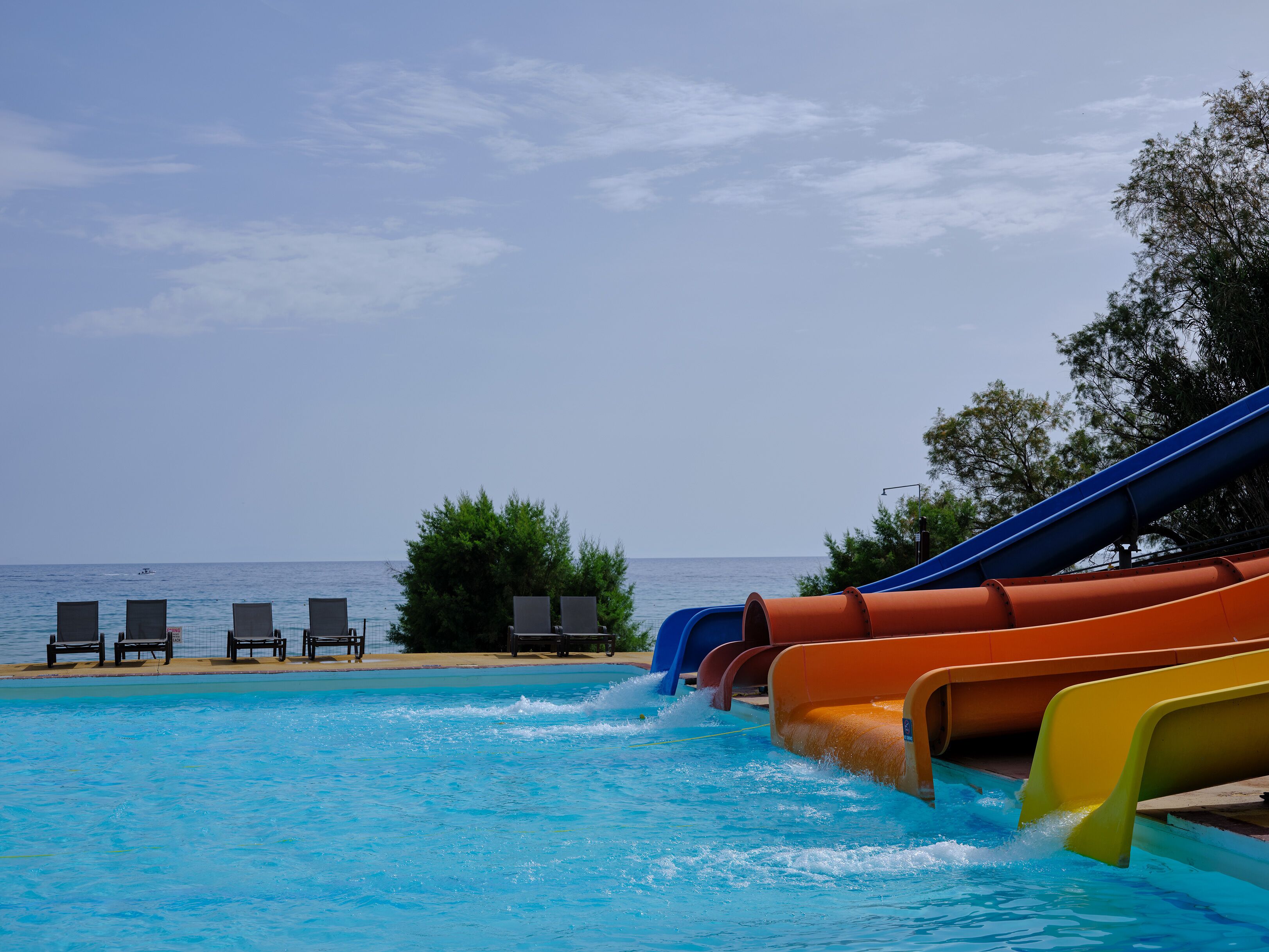 Ein Swimmingpool mit mehreren Wasserrutschen, Liegestühlen und Blick auf das Meer.