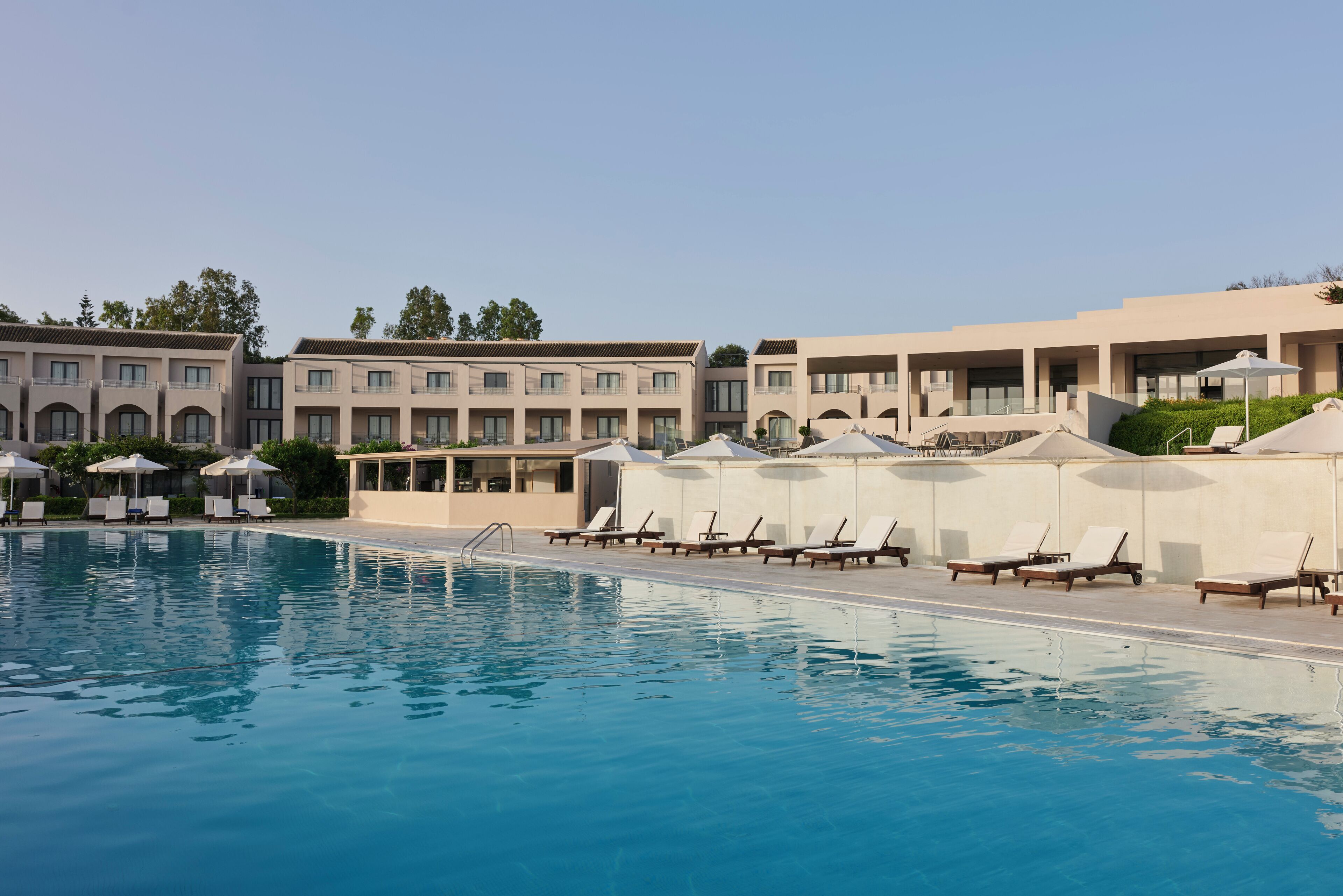 A swimming pool with lounge chairs and umbrellas, surrounded by multi-story buildings with balconies and large windows.