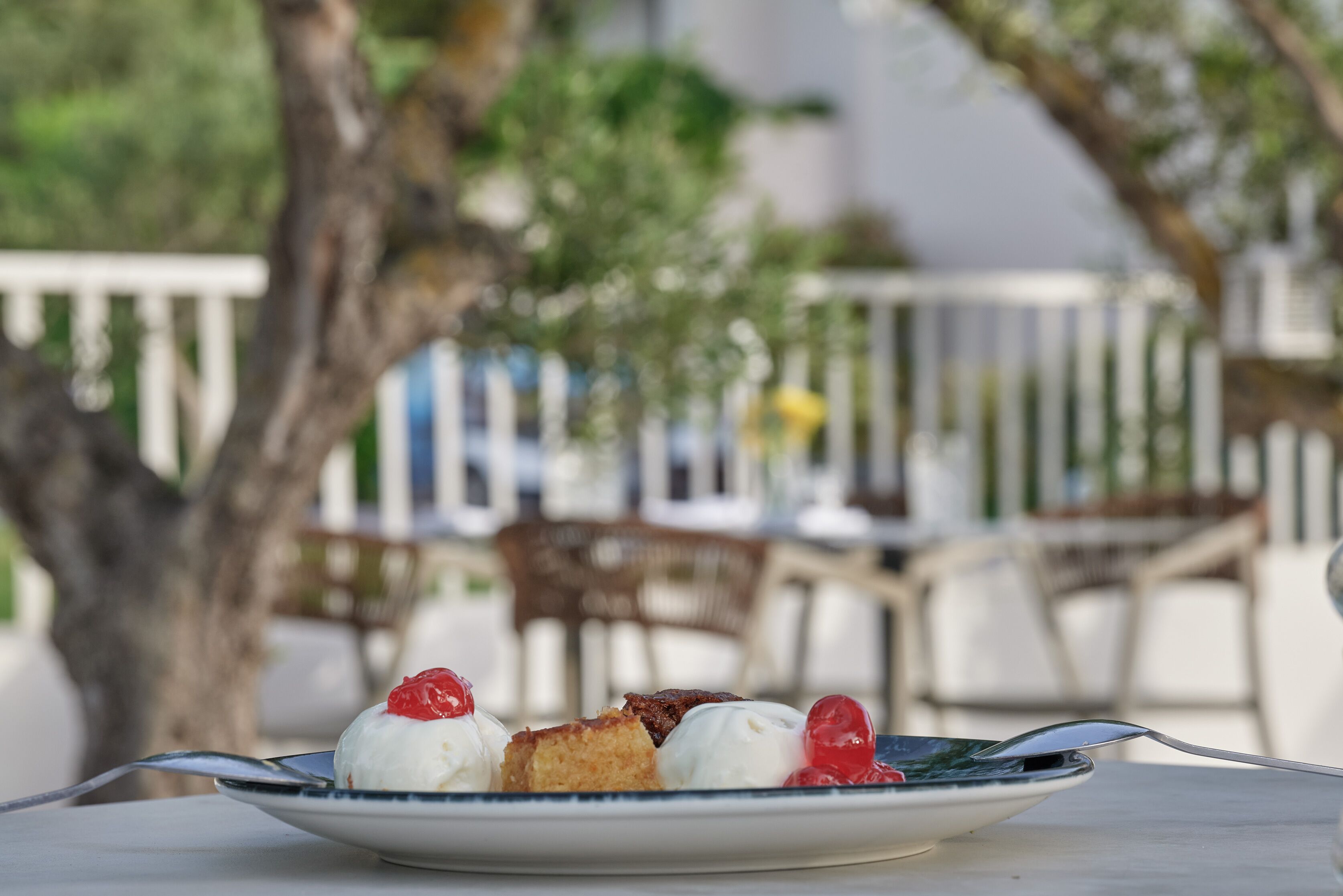 A plate of dessert with a fork on a table in an outdoor setting with chairs and a tree in the background.