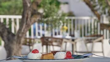 A plate of dessert with a fork on a table in an outdoor setting with chairs and a tree in the background.