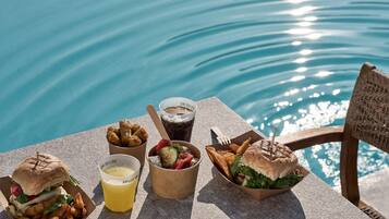 Une table dressée avec une variété de plats, notamment un hamburger, des frites, une salade et une boisson, le tout disposé devant une vue sur la piscine.