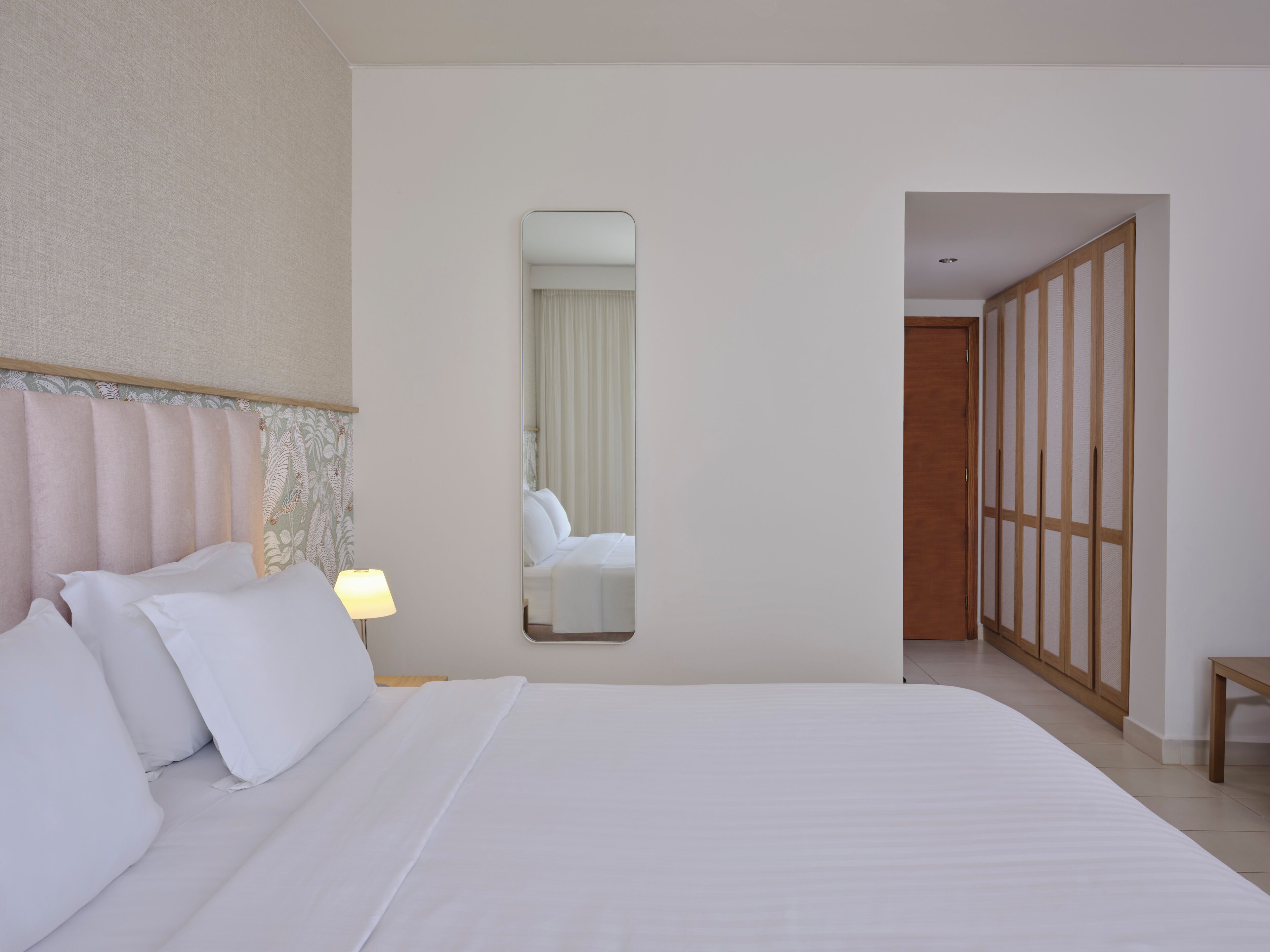 Une chambre d’hôtel avec un grand lit, une lampe de chevet, un miroir et une armoire.