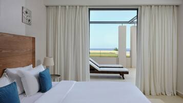 A hotel room with a large bed, a wooden headboard, a nightstand, a lamp, and a view of the beach through the window.