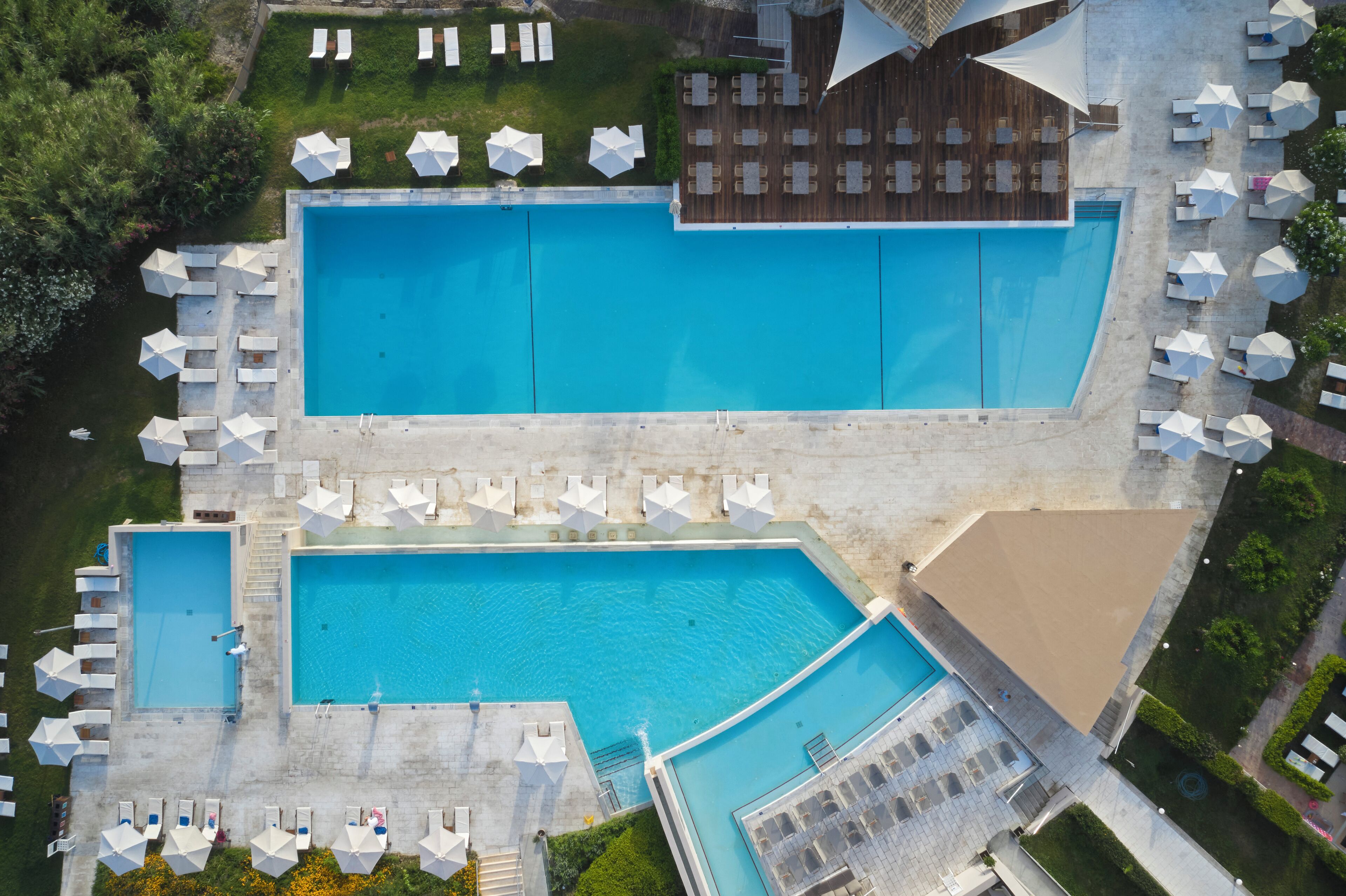 Vista aérea de un hotel con dos piscinas grandes, numerosas tumbonas y una zona de estar cubierta.