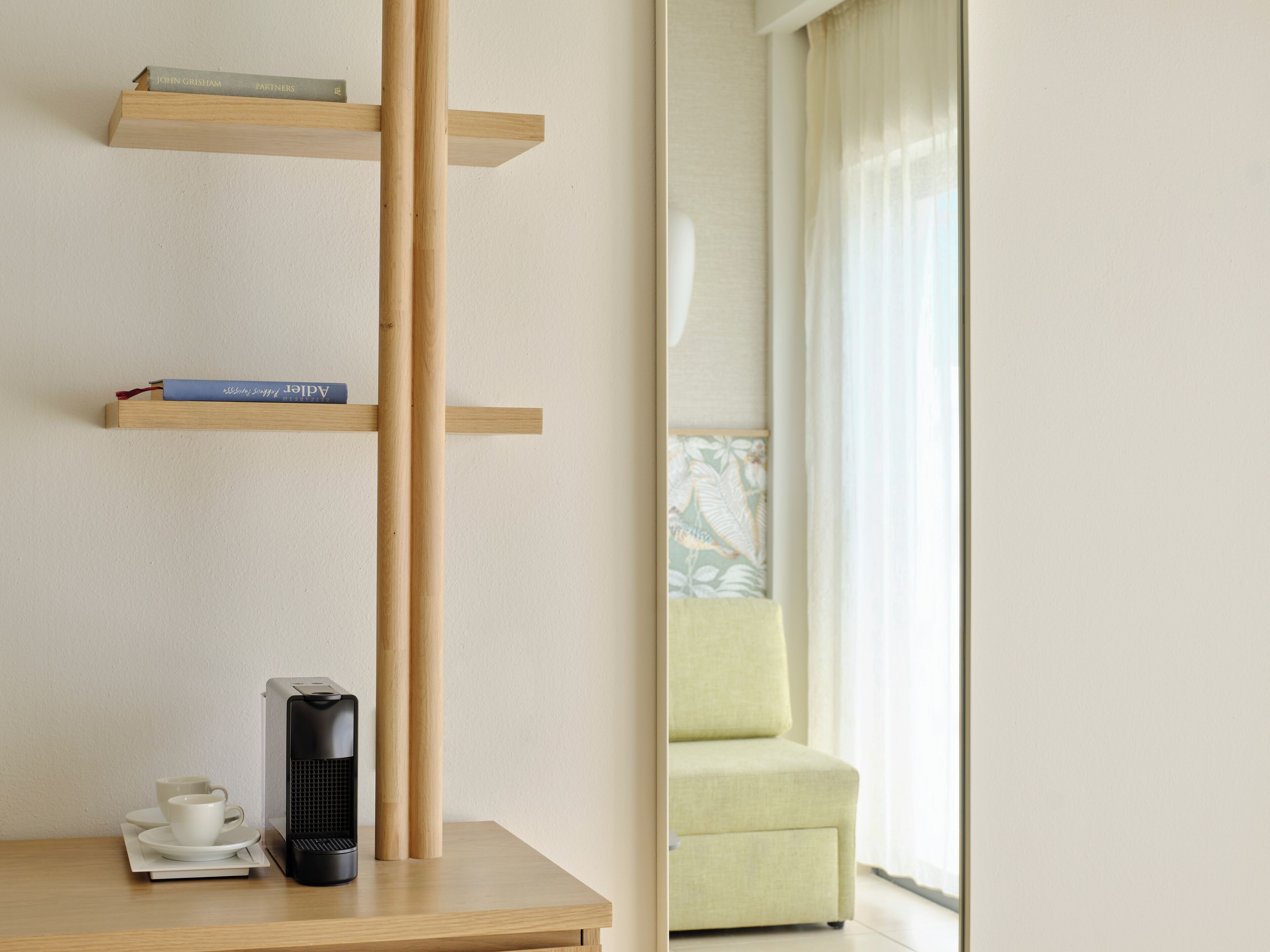 Una habitación minimalista con una mesa de centro de madera, una cafetera negra y una estantería llena de libros.