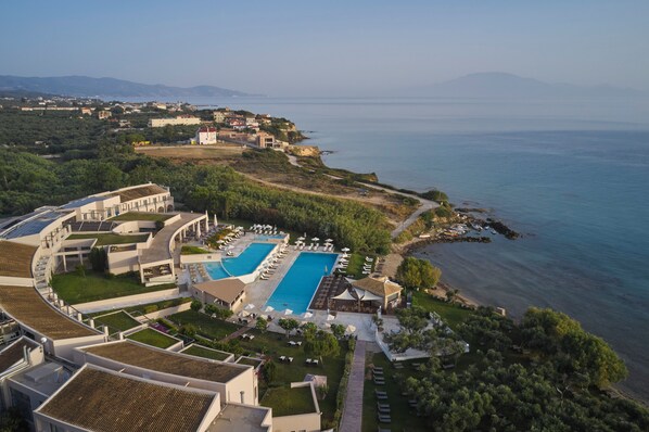 A resort with a large swimming pool, multiple guest rooms, and a scenic coastal view.
