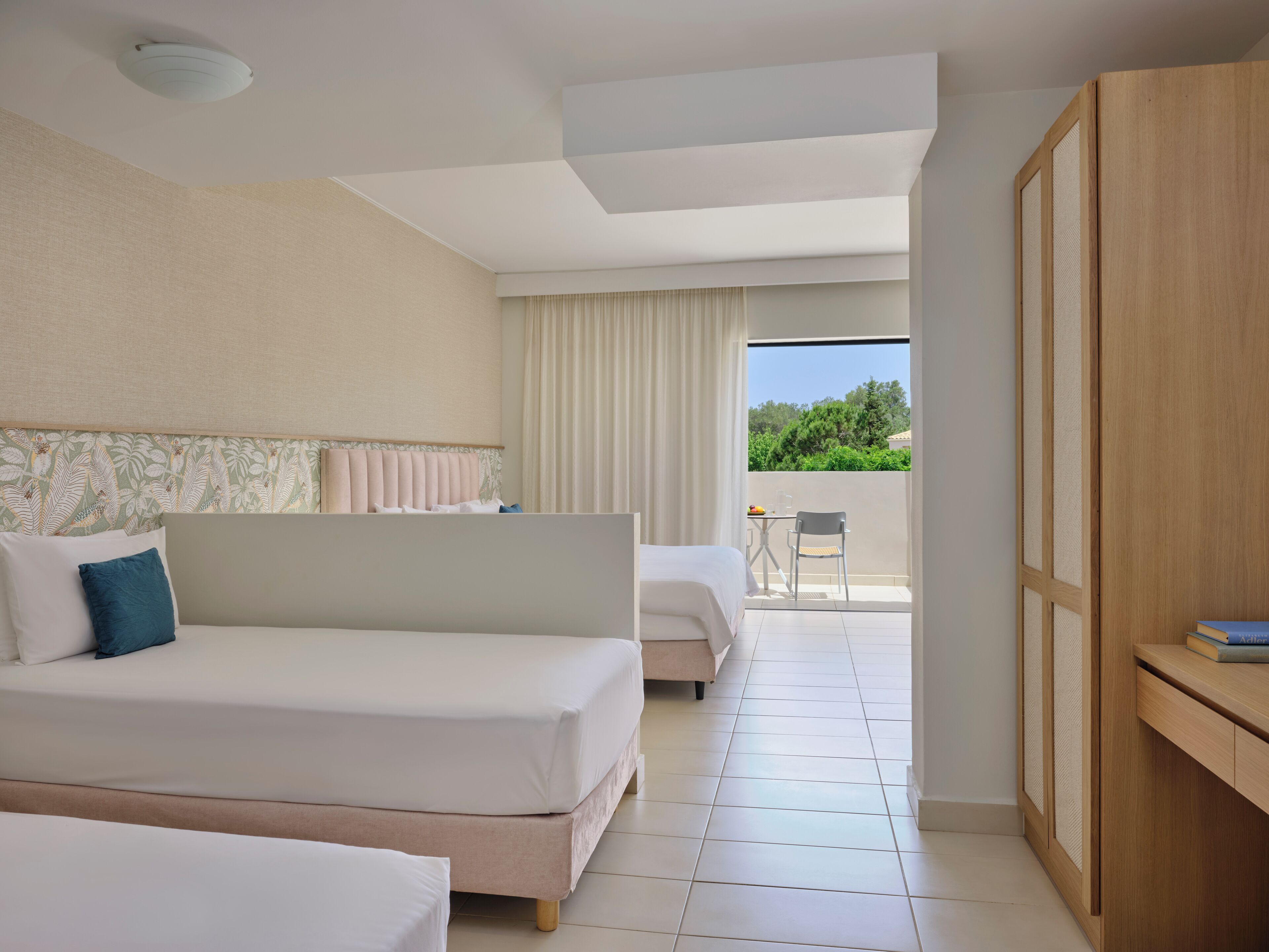 Habitación de hotel con dos camas, un balcón con mesa y silla, y un armario.